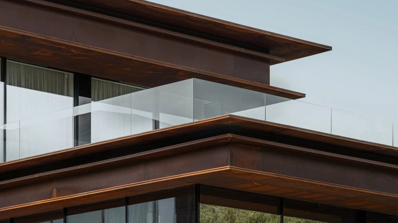 Close detail of a cantilevered bronze toned roofline meeting a glass balcony edge against open sky on a Coconut Grove residence