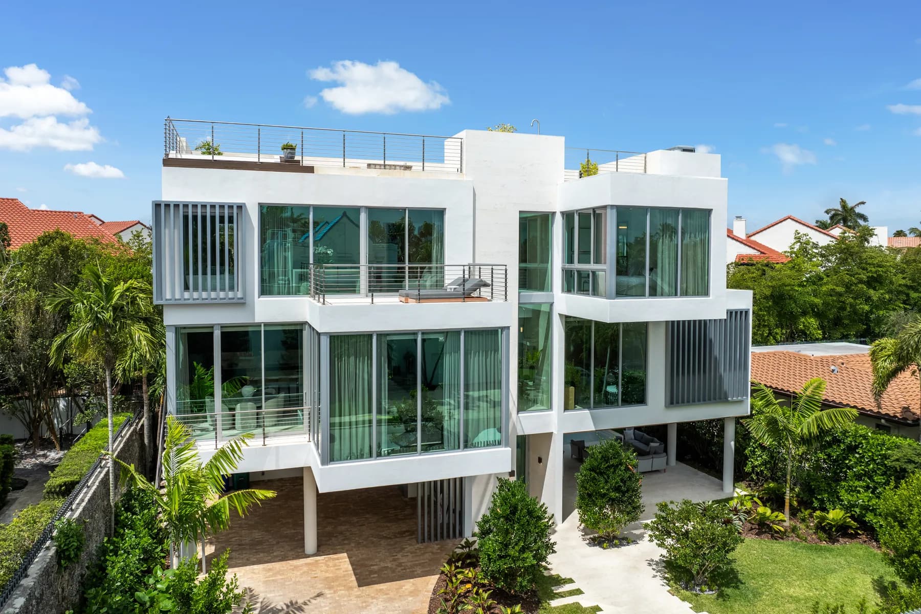 Three-story modern Coconut Grove residence with white stucco volumes, glass walls and cantilevered balconies set among mature palms, showing the kind of proportion a design decision locks in before any furniture is chosen